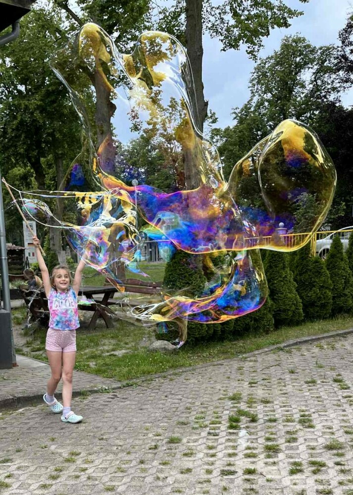 Fotografia przedstawia dziewczynkę puszczającą ogromne bańki mydlane.