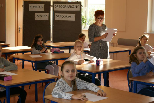 dzieci siedzą osobno przy każdej ławce, a na ławkach przed nimi leżą kartki