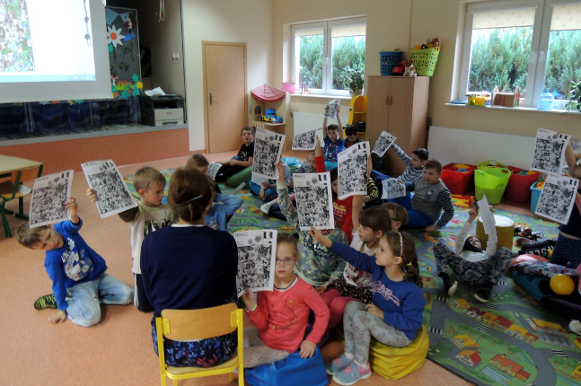 dzieci siedzą na podłodze i prezentują pani obrazek