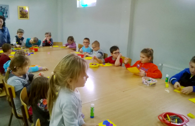 dzieci tworzą prace plastyczne przy długim stole