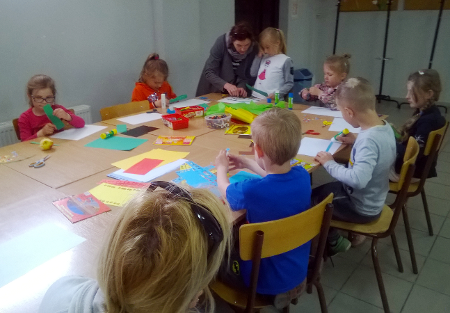 dzieci tworzą prace plastyczne przy długim stole