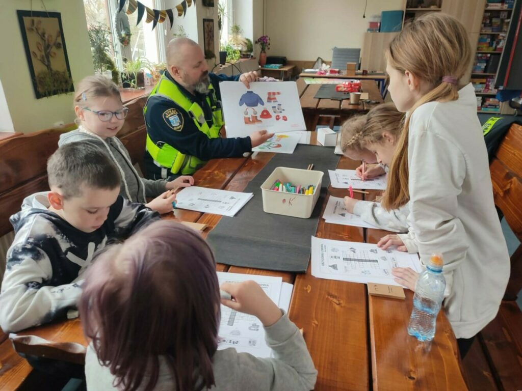 Fotografia przedstawia grupę dzieci słuchających pana ze Straży Gminnej.