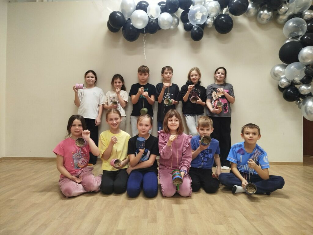 Grupowe zdjęcie dzieci biorących udział w feriach zimowych w Klubie w Dołujach – uczestnicy uśmiechnięci, trzymają własnoręcznie wykonane karmniki z puszek, wypełnione mieszanką karmy dla ptaków, płatkami owsianymi i smalcem