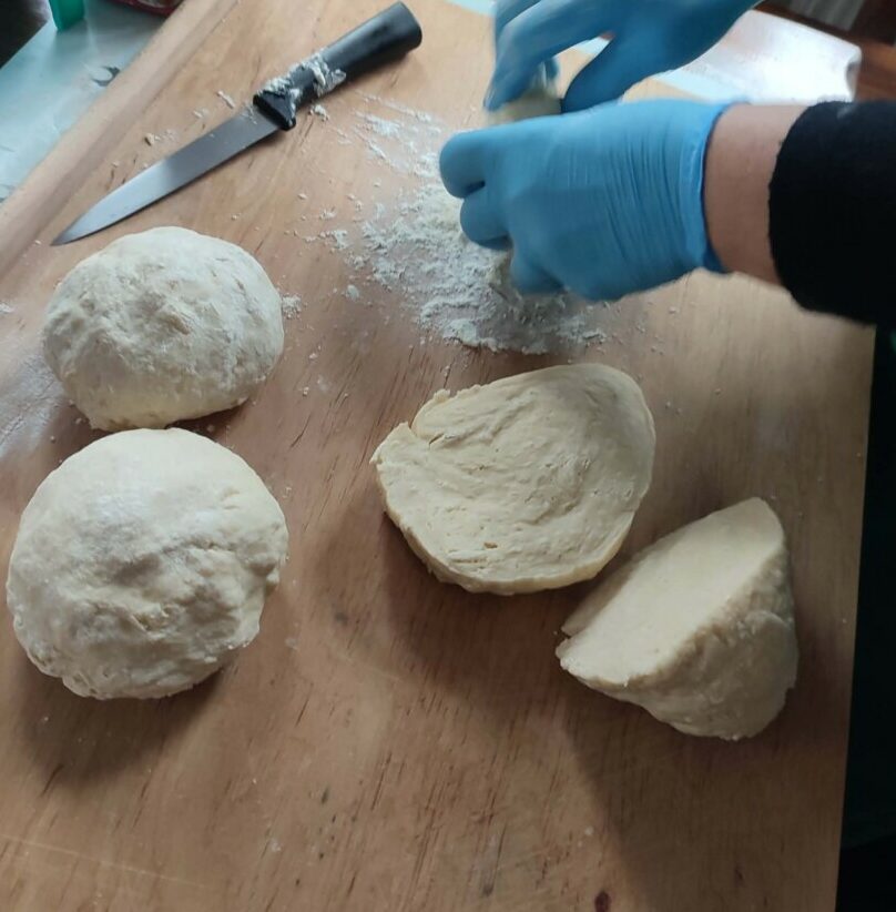 Fotografia przedstawia panią, która kroi ciasto na drewnianej stolnicy.