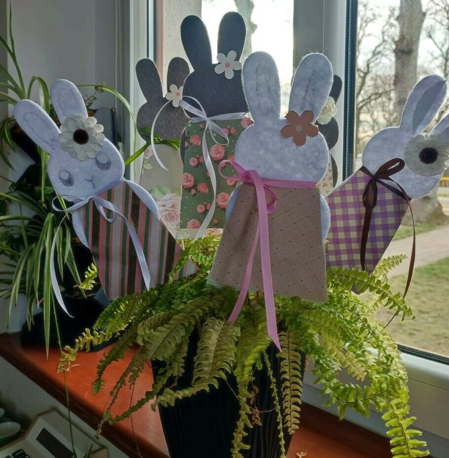 Fotografia przedstawia małe sylwetki zajączków na patyczkach umieszczone w paprotce.