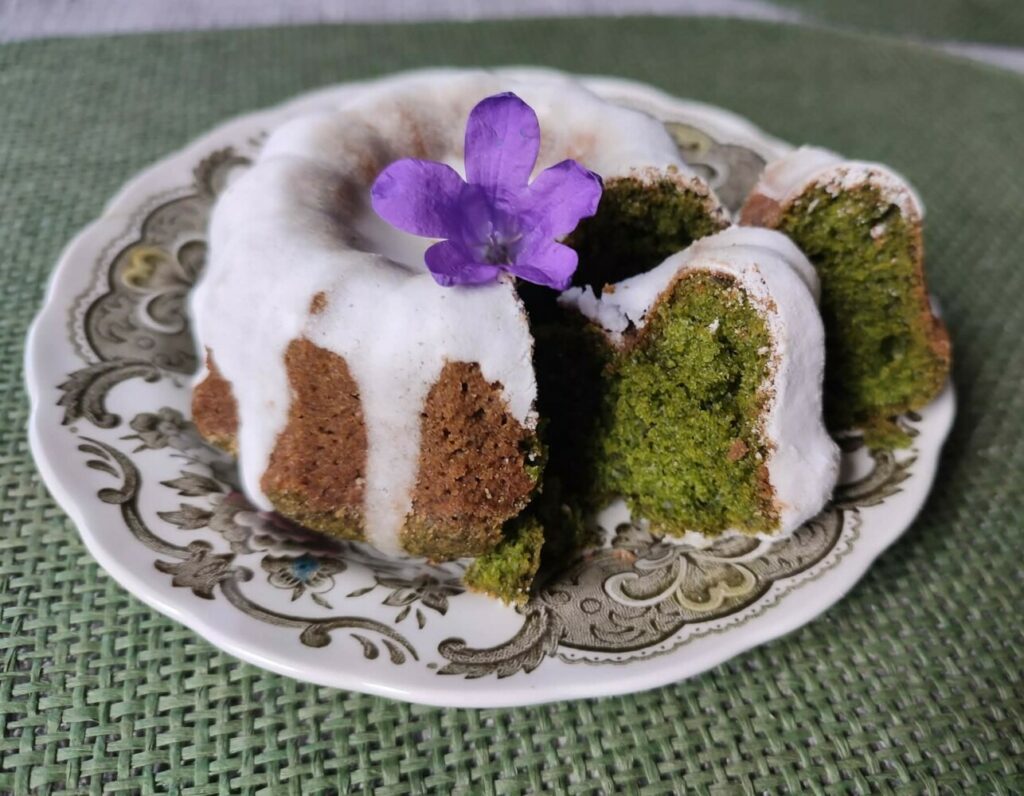Fotografia przedstawia zieloną mini babeczkę udekorowaną białym lukrem.