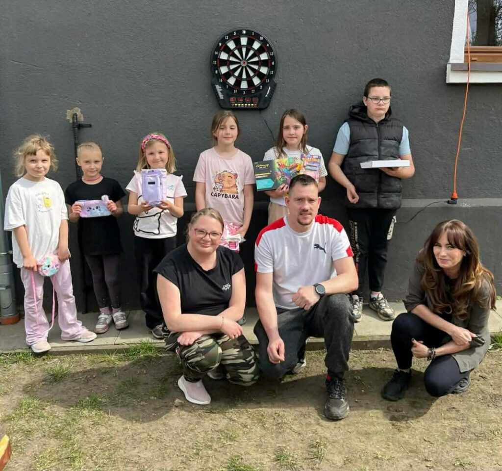 Fotografia przedstawia grupę dzieci oraz opiekunów przy tarczy do gry w darta.
