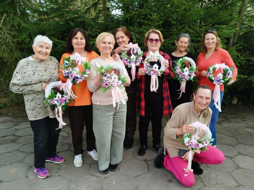 Uczestniczki warsztatów „Wiosenne wianki” dla seniorów w GCKiB w Dołujach prezentują własnoręcznie wykonane dekoracyjne wianki.