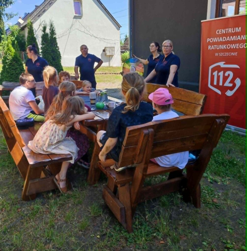 Fotografia przedstawia grupę dzieci oraz kilka osób dorosłych (operatorów Numeru Alarmowego 112.