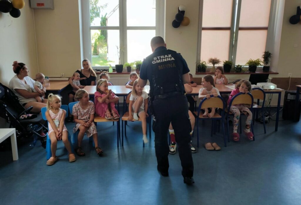 Fotografia przedstawia grupę dzieci, przed którymi stoi funkcjonariusz Straży Gminnej.