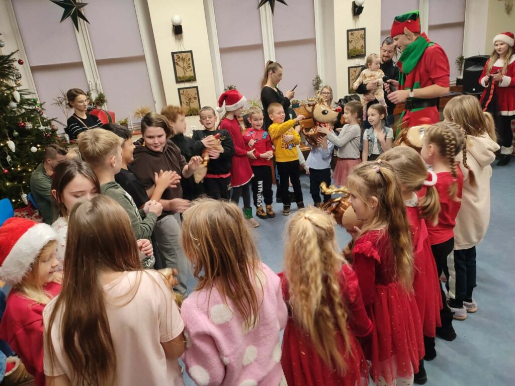 Fotografia przedstawia grupę dzieci bawiących się i tańczących z elfem.