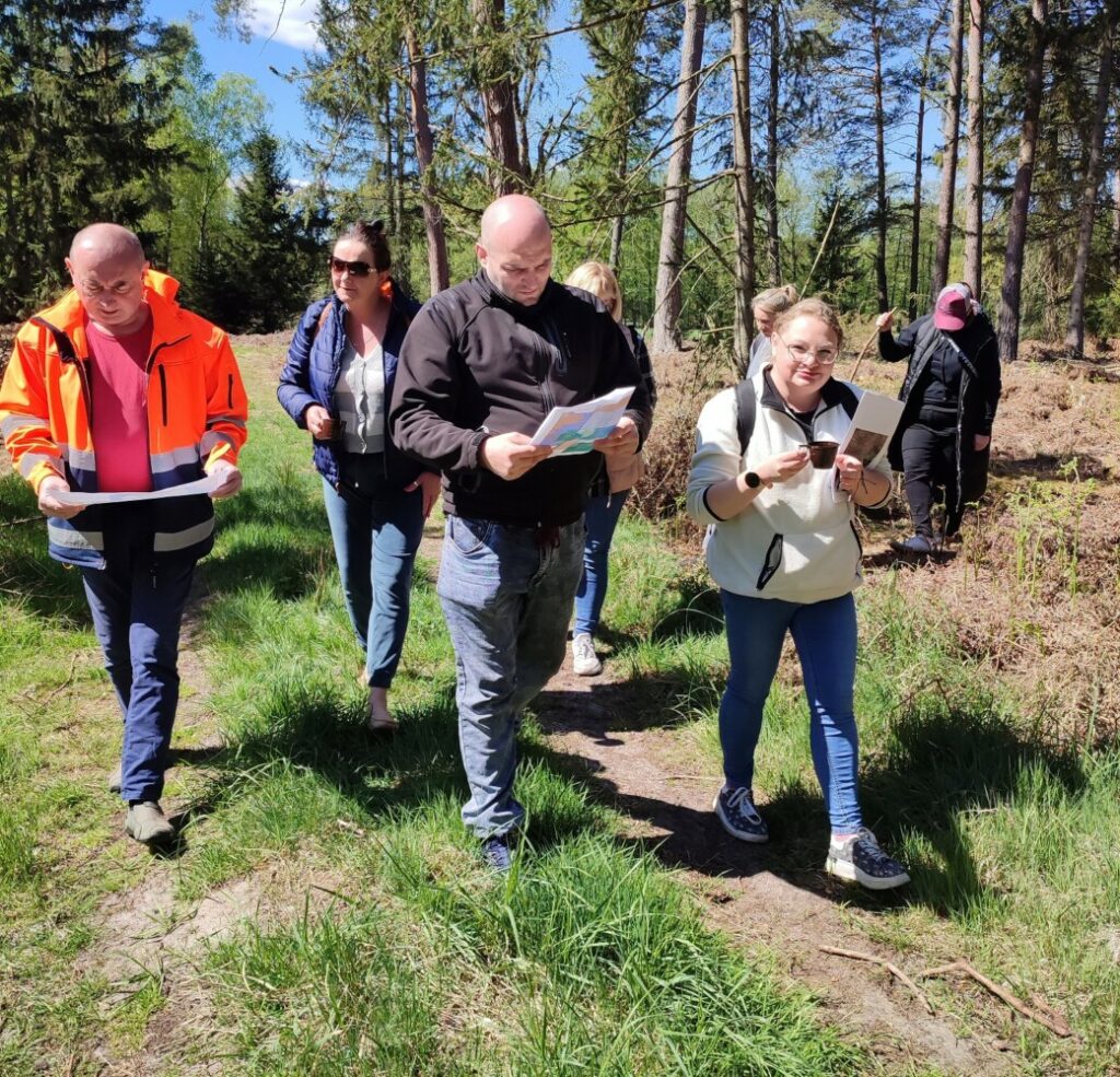 Fotografia przedstawia grupę osób spacerujących po lesie.