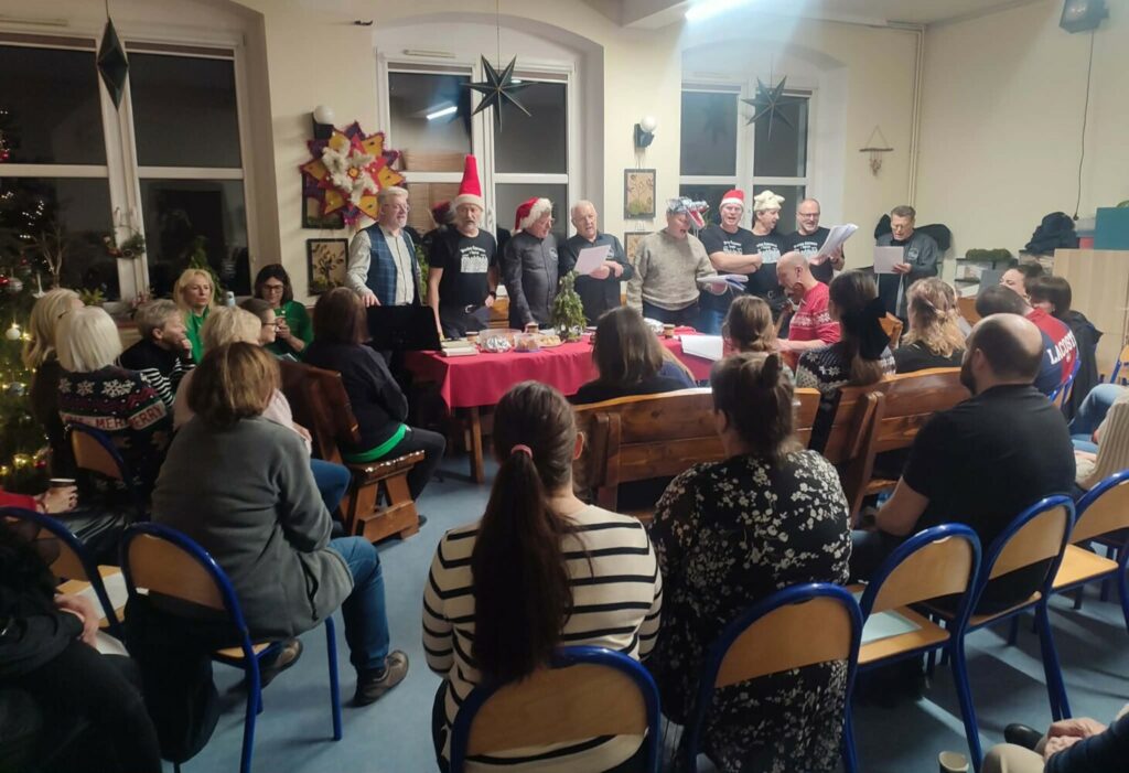 Fotografia przedstawia grupę śpiewających mężczyzn z gwiazdą kolędniczą w tle.