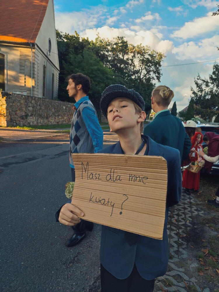 Fotografia przedstawia chłopca trzymającego kartkę z napisem: "Masz dla mnie kwiaty ?".