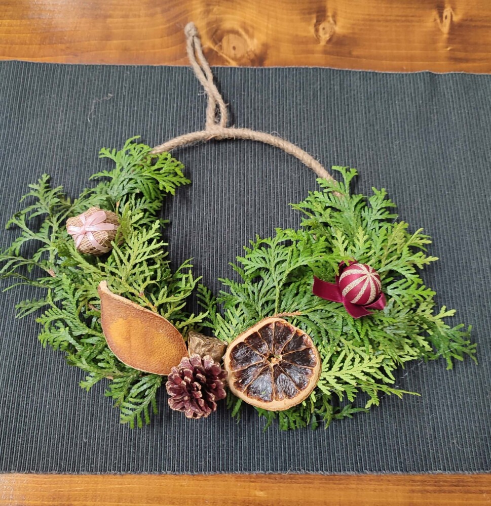 Fotografia przedstawia stroik świąteczny - kółko w kształcie bombki z naturalnymi gałązkami.